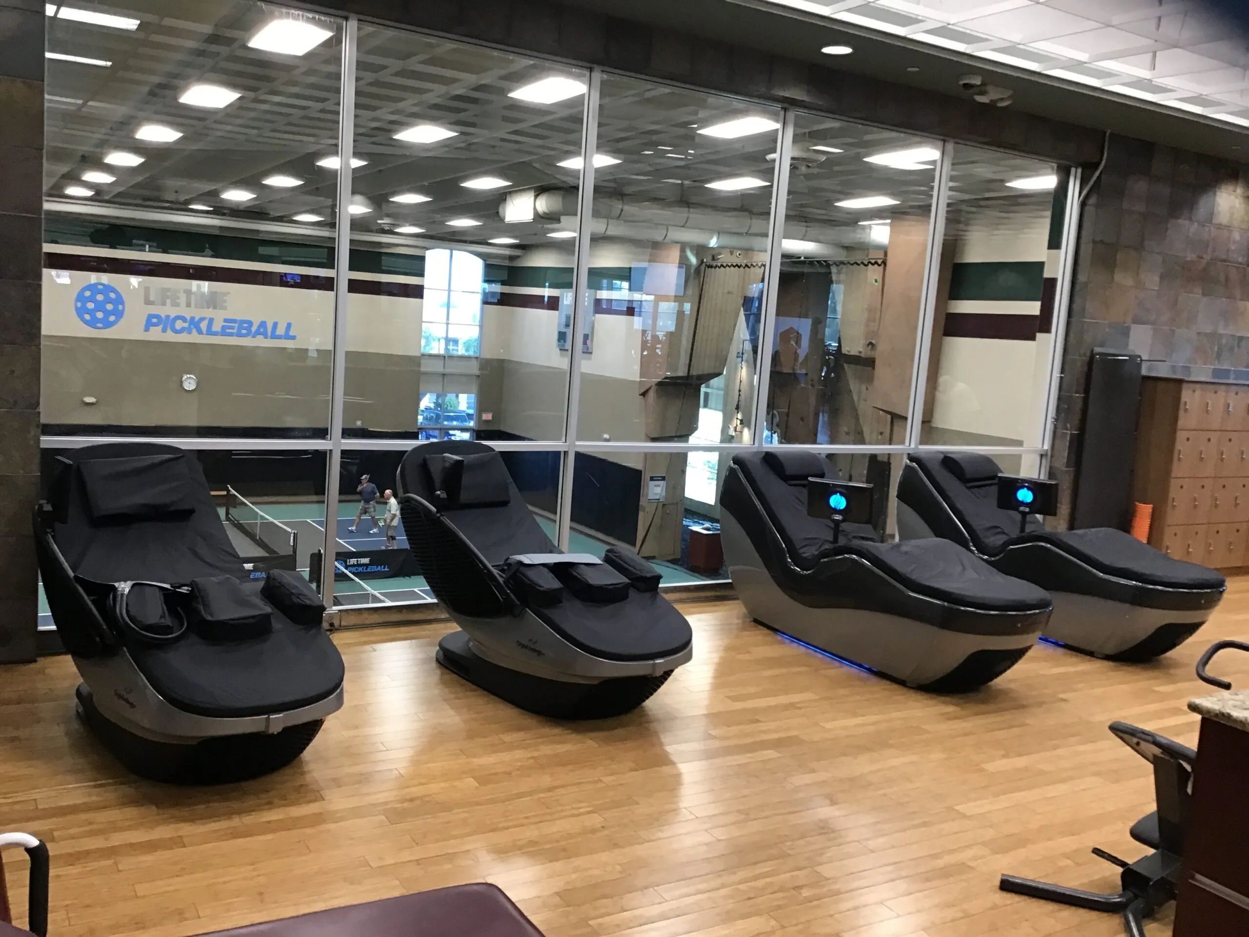 Muscle Recovery 9 Two CryoLounge+ chairs and two HydroMassage lounges facing a window that overlooks indoor pickleball courts