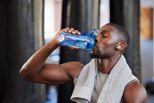 Man with a towel around his neck drinking water from a blue bottle after a workout