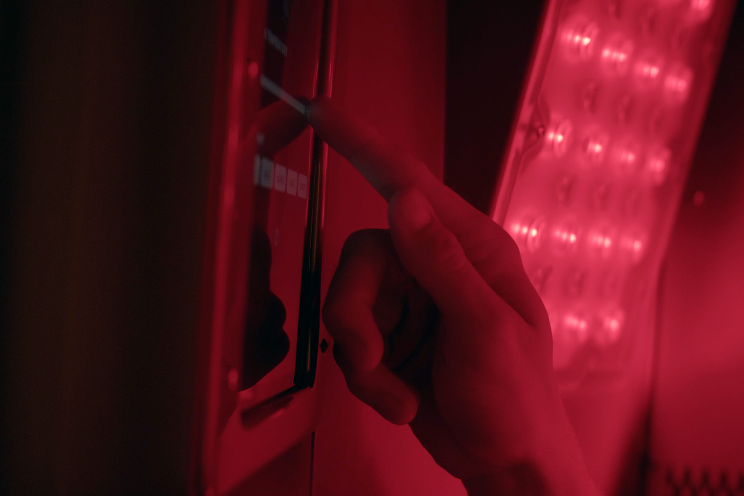 Product - RedZone Sauna 4 Hand pressing controls on the sauna’s interior touchscreen beside a glowing red LED panel.